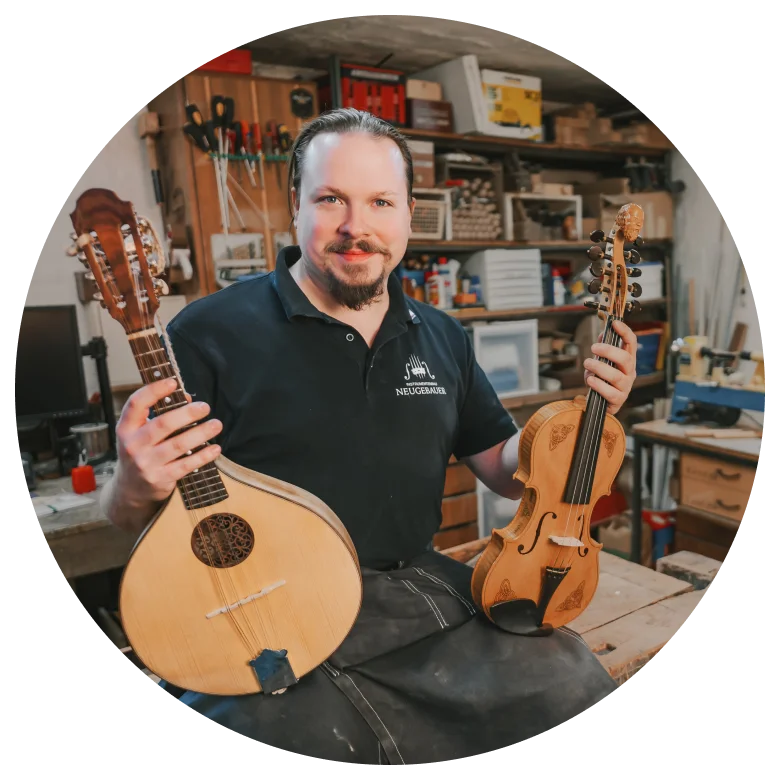 Lukas Neugebauer in seiner Werkstatt mit Instrumenten in der Hand, lächelnd